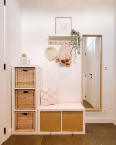 a white entryway with baskets and hanging items on the wall next to a bench