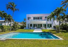 a large white house with a pool in the front yard and palm trees surrounding it