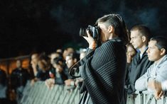 a woman taking a photo with her camera in front of a group of people behind a fence