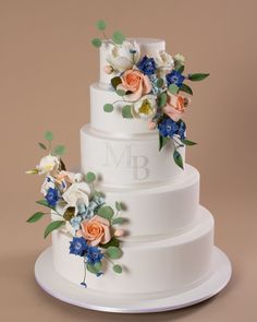 a three tiered white wedding cake with blue and peach flowers on the top layer