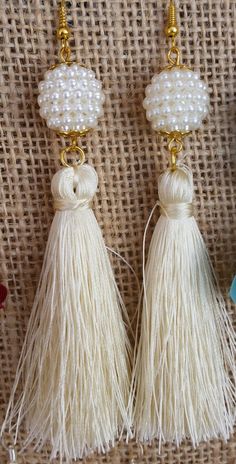 two white tasselled earrings with pearls and beads on top of a piece of cloth