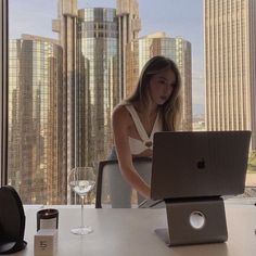 a woman sitting in front of a laptop computer on top of a desk next to a window