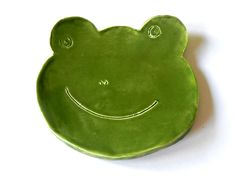 a green frog shaped plate with a smiley face on it's side, against a white background