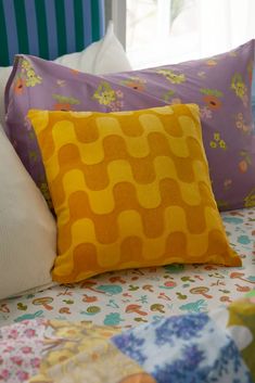 a bed topped with lots of pillows next to a colorful headboard and window sill