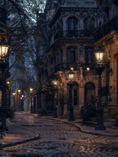 an empty cobblestone street at night with lanterns on the buildings and trees in the background