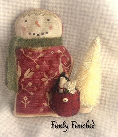 a knitted snowman with a red bag and small white tree