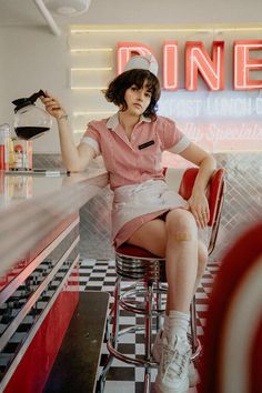 a woman sitting on top of a stool in front of a neon sign and holding a cell phone