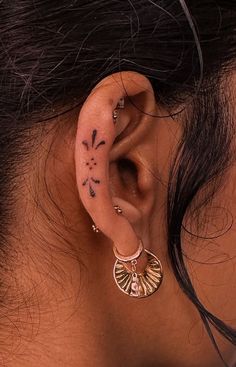 a woman's ear with tattoos on it and an ear piercing in the middle