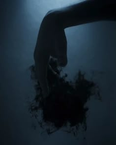 a person's hand reaching for something in the water with dark blue light shining on them