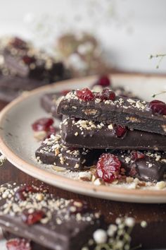 three pieces of chocolate with cranberries and nuts are on a plate next to some flowers