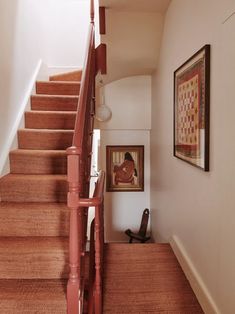 there is a painting on the wall next to the stairs in this house with red carpet