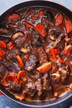 a pot filled with stew and carrots on top of a blue tablecloth next to a spoon