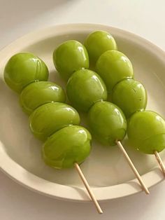 some green fruit on a white plate with toothpicks in it's middle