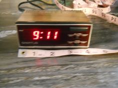 an alarm clock sitting on top of a table next to a measuring tape and scissors