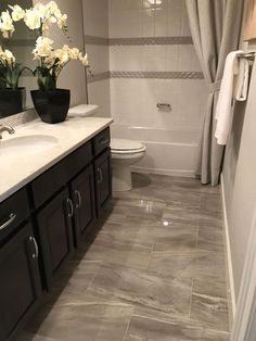 a bathroom with white flowers in a black vase on the counter and gray tiles on the floor