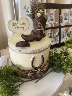 there is a cake with a cowboy boot on the top and greenery around it