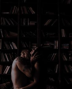 a shirtless man sitting in front of a bookshelf