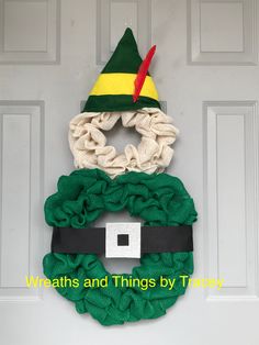 a green wreath with a yellow and red hat on it hanging from the front door