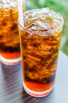 two glasses filled with ice tea sitting on top of a table