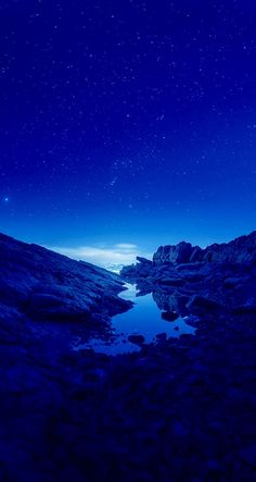 the night sky with stars above some rocks and water in the foreground is a mountain range