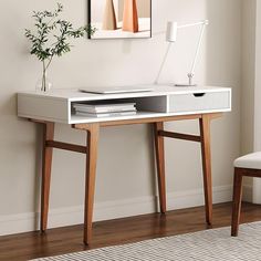 a white desk with a laptop on it in front of a wall mounted painting and chair