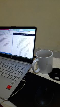 an open laptop computer sitting on top of a desk next to a cup and mouse