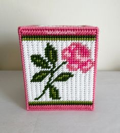 a pink and white basket with a flower on the front is sitting on a table