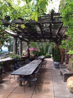 a wooden table sitting under a pergoline covered roof next to potted plants