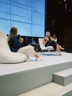 two women are sitting in chairs and talking on the phone while another woman is standing behind them