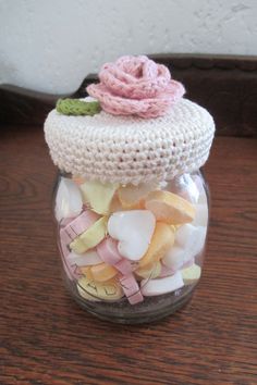 a glass jar filled with candy and a pink rose on top of the lid is sitting on a wooden table