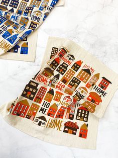 two tea towels with houses on them and the words home printed on them are laying next to each other