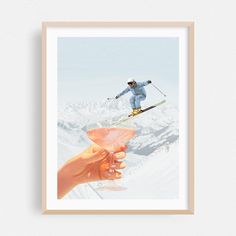 a hand holding a wine glass in front of a photo of a person on skis