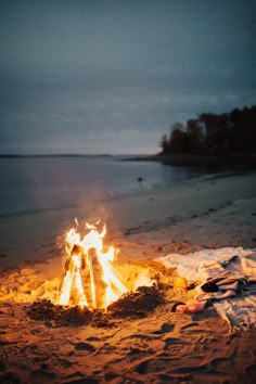 a campfire is lit on the beach at night