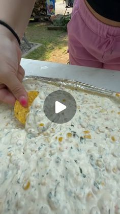 a person is placing corn on top of some food in a pan with another hand