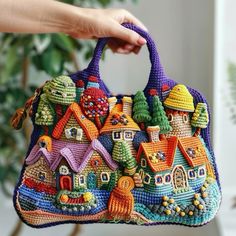 a crocheted purse with houses and trees on it is being held by a woman