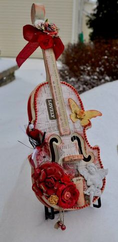 an altered violin is sitting in the snow with red ribbon on it's neck