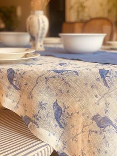 a blue and white table cloth with birds on it sitting on a dining room table