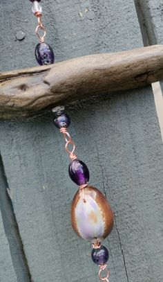 a long beaded necklace with purple and white beads hanging from a piece of wood