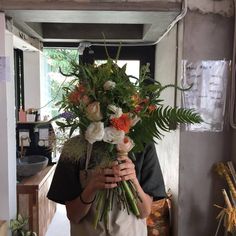 a man holding a bunch of flowers in front of his face and looking at the camera