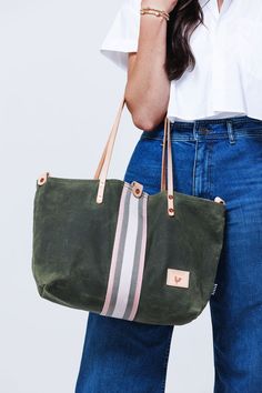 Model displaying brushed leather olive green tote with cream and grey accent stripes down the center and cream colored shoulder straps. Work Bag Essentials, Leather Strap Bag, Wax Canvas, Lynchburg Virginia, Waxed Canvas Bag, Limited Edition Bag, Canvas Bags, Webbing Strap, Chic Bags