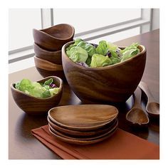 three wooden bowls filled with lettuce on top of a table next to utensils