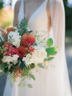 a bride holding a bouquet of flowers and greenery