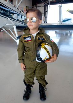 a young boy in an air force pilot's uniform holding a ball and helmet