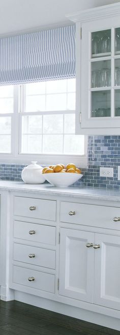 a kitchen with white cabinets and blue tile backsplash, window blinds in the back