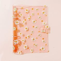 a pink notebook with white daisies and orange spiral binders on top of it