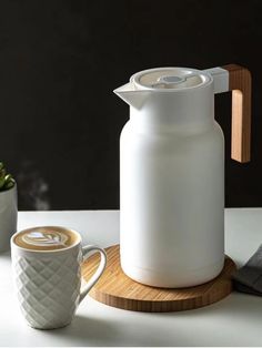 a white jug sitting on top of a wooden coaster next to a cup and saucer