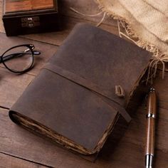 an old book with a pen and eyeglasses on a wooden table next to a pair of glasses