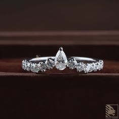 a white gold ring with three pear shaped diamonds on the top and bottom, sitting in a wooden box