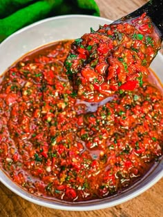 a spoon full of chili sauce on top of a white bowl filled with green peppers