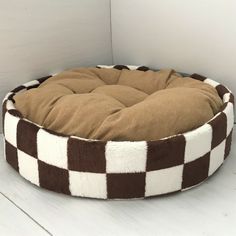 a brown and white checkered dog bed sitting on top of a wooden floor next to a wall